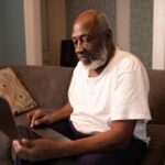 elderly man sits using a laptop