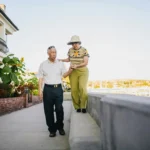 Man and Woman Walking on Gray Concrete Bench