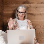 Elderly woman using a laptop for a video call, relaxing indoors.
