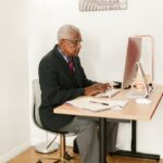 Elderly man in suit typing on desktop in an office setting. Professional workspace.