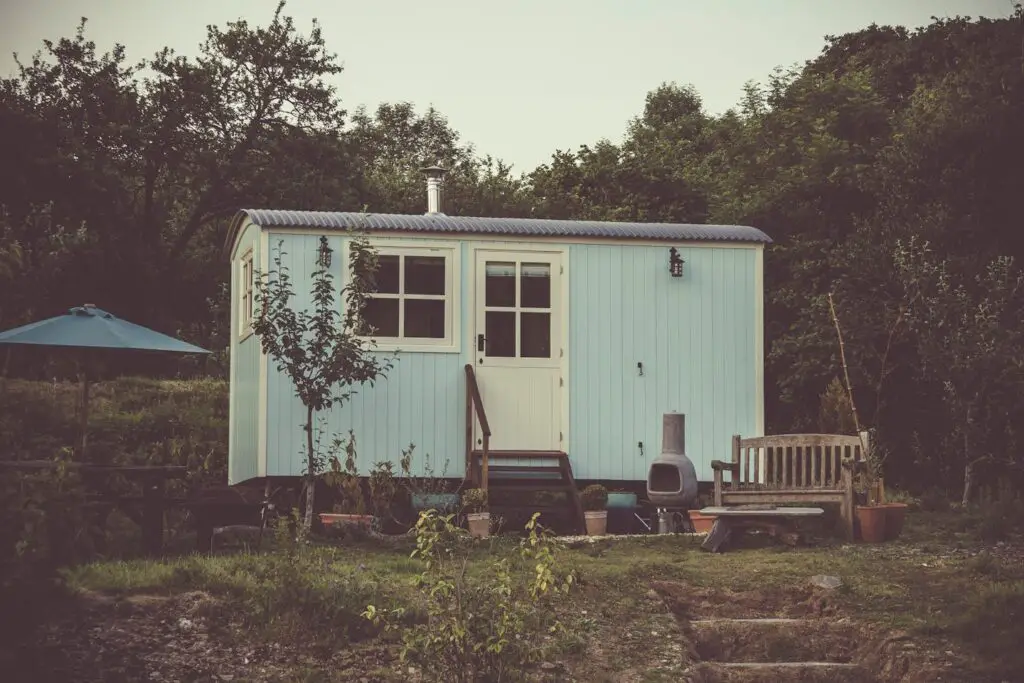 A cozy and rustic tiny house in the countryside with outdoor seating and lush greenery.