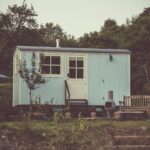 A cozy and rustic tiny house in the countryside with outdoor seating and lush greenery.