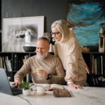 Elderly couple using a laptop at home, enjoying online activities and companionship.