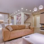 Luxurious living room with modern interior design, featuring beige sofa, fireplace, and open kitchen.