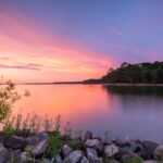 calm water near green trees during sunset