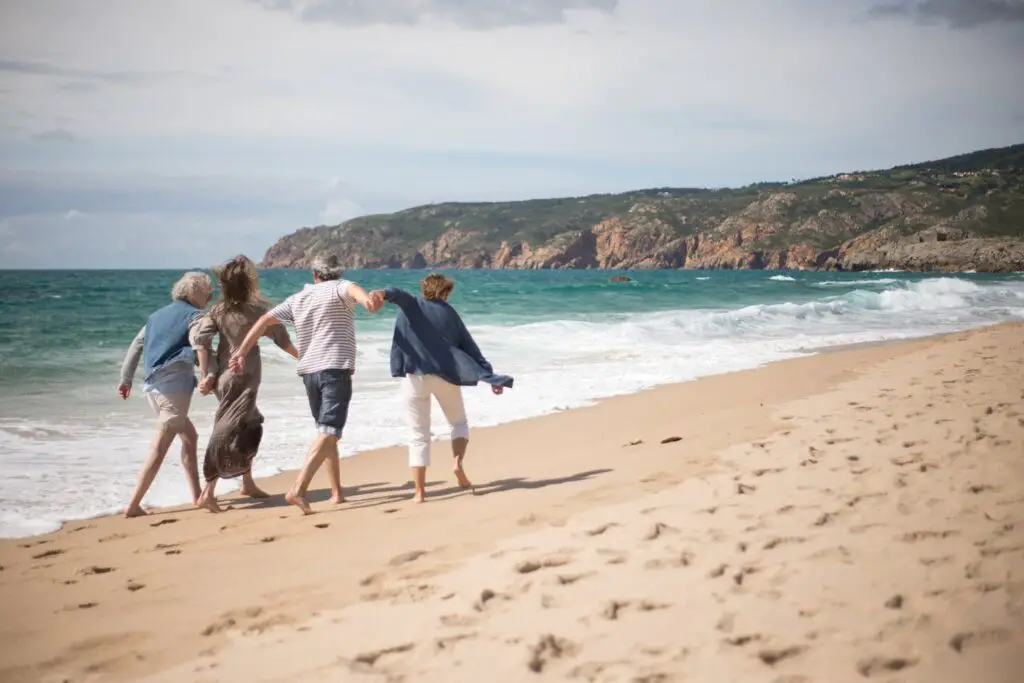 Senior adults walking on a scenic beach in Portugal, enjoying a sunny day by the sea.