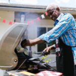 Senior man barbecuing outside on a sunny day, enjoying cooking on a grill.