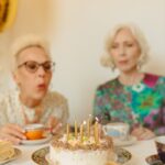 Two senior women enjoying a celebration indoors with a cake.