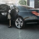 Senior businesswoman stepping out of a sleek black luxury vehicle in a cityscape.