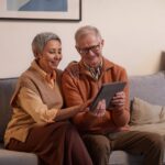 Happy senior couple sitting together on a sofa using a tablet indoors.
