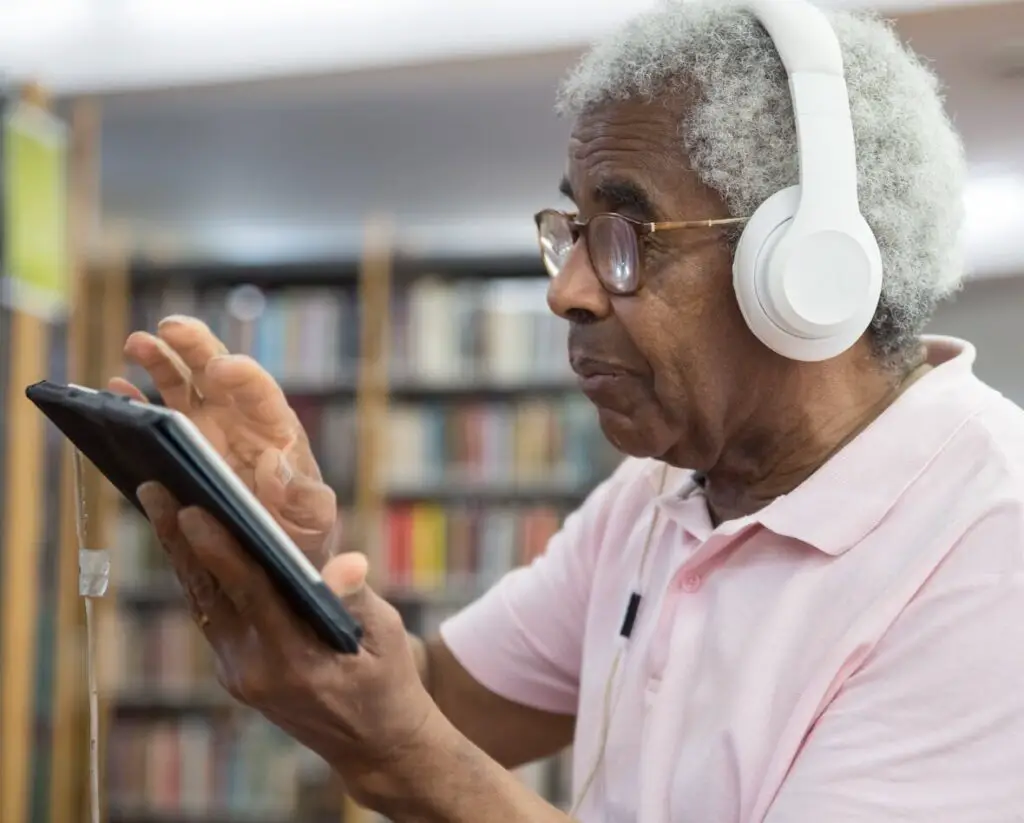Elderly man with headphones explores digital content on a tablet in a library.