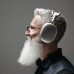 Side profile portrait of a mature man with a beard and wireless headphones against a neutral background.